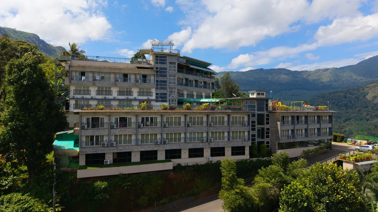 The Munnar Queen in daylight, its terraces stepping down the hillside under the ranges