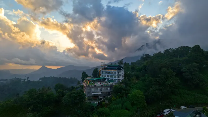 The Munnar Queen on its forested hilltop at dusk, with sunlit cloud breaking over the ranges