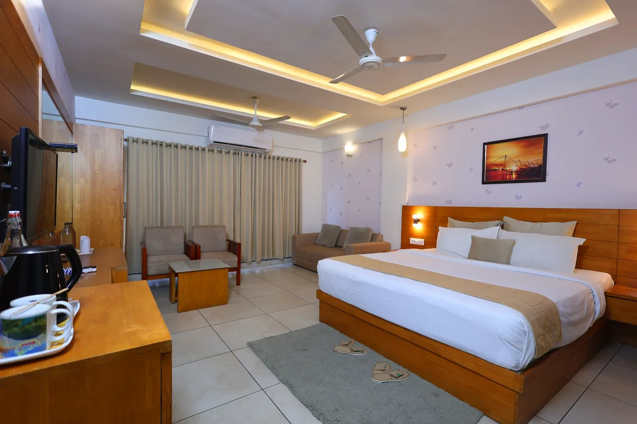 A spacious room with a double bed, a sofa set and curtained balcony doors