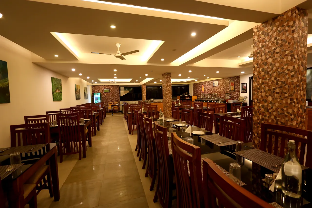 The restaurant at The Munnar Queen, wooden chairs and tables under a lit ceiling